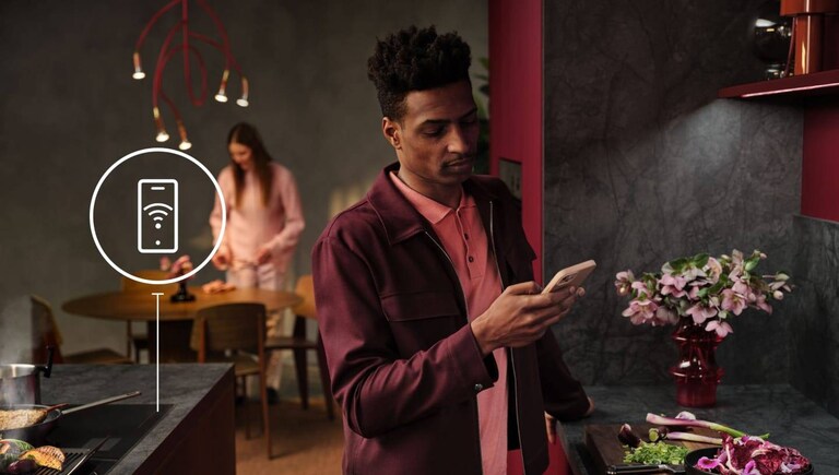 A man is looking at his phone in the kitchen. 