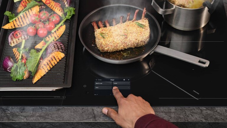 A finger is touching the control panel on an induction hob.