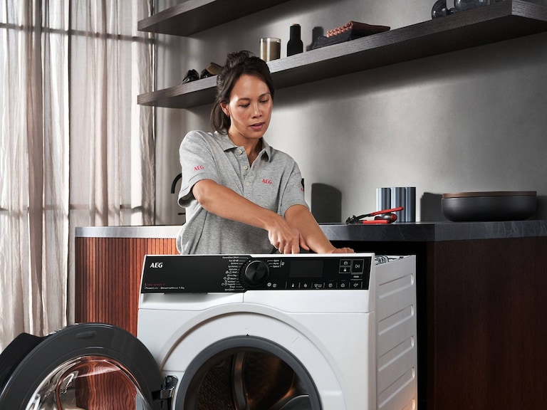 Service technician repairing Washing Machine in front of dark gray shelves