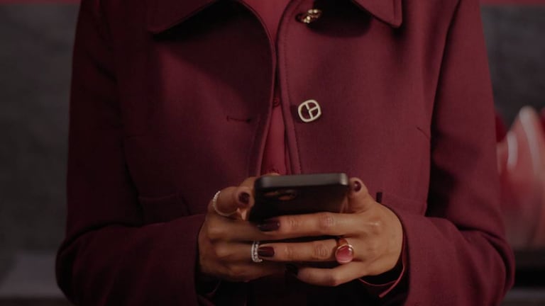 Close-up of person in deep red coat, painted nails and rings using mobile phone