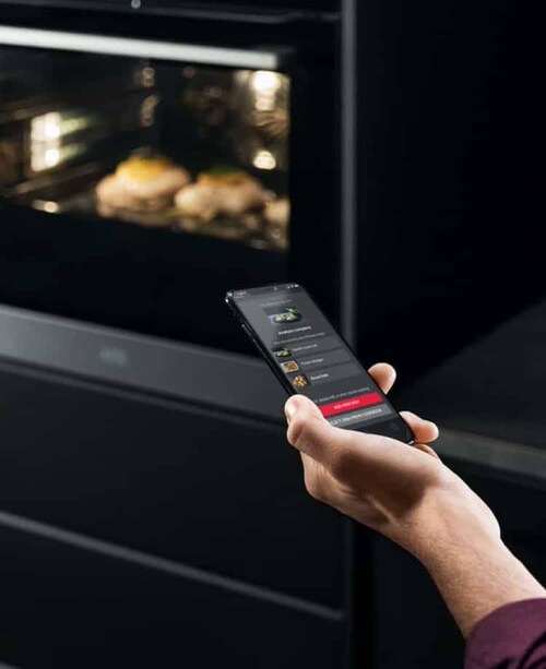 A hand with a smartphone in front of a oven