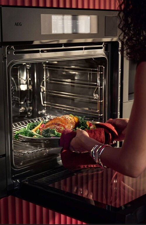 Women using a steam oven pulling out a tray from the oven